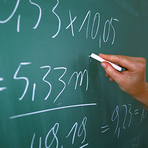 Auf dem Bild eine Tafel, wo eine Hand zu sehen ist, die mit Kreide Zahlen schreibt